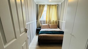 A narrow hallway leading to a bedroom with a bed, curtains, and a small table. - Entire 4-bed House in Sunderland (Sunderland)
