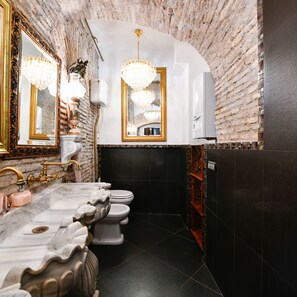 A luxurious bathroom with a marble sink, gold fixtures, and a brick wall.