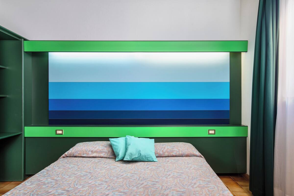 Une chambre à coucher avec un lit, une tête de lit verte et un grand tableau abstrait accroché au mur.