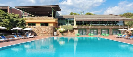 Piscina con sillas de descanso y sombrillas, rodeada por un muro de piedra y un edificio con amplias ventanas.