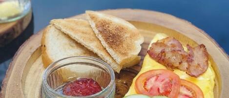 A breakfast plate with toast, bacon, eggs, tomatoes, and a small bowl of jam.