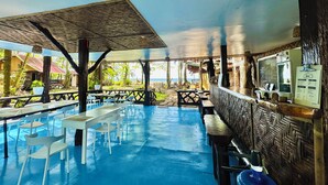 Zona de piscina al aire libre con mesas, sillas, un bar y vistas a la playa.