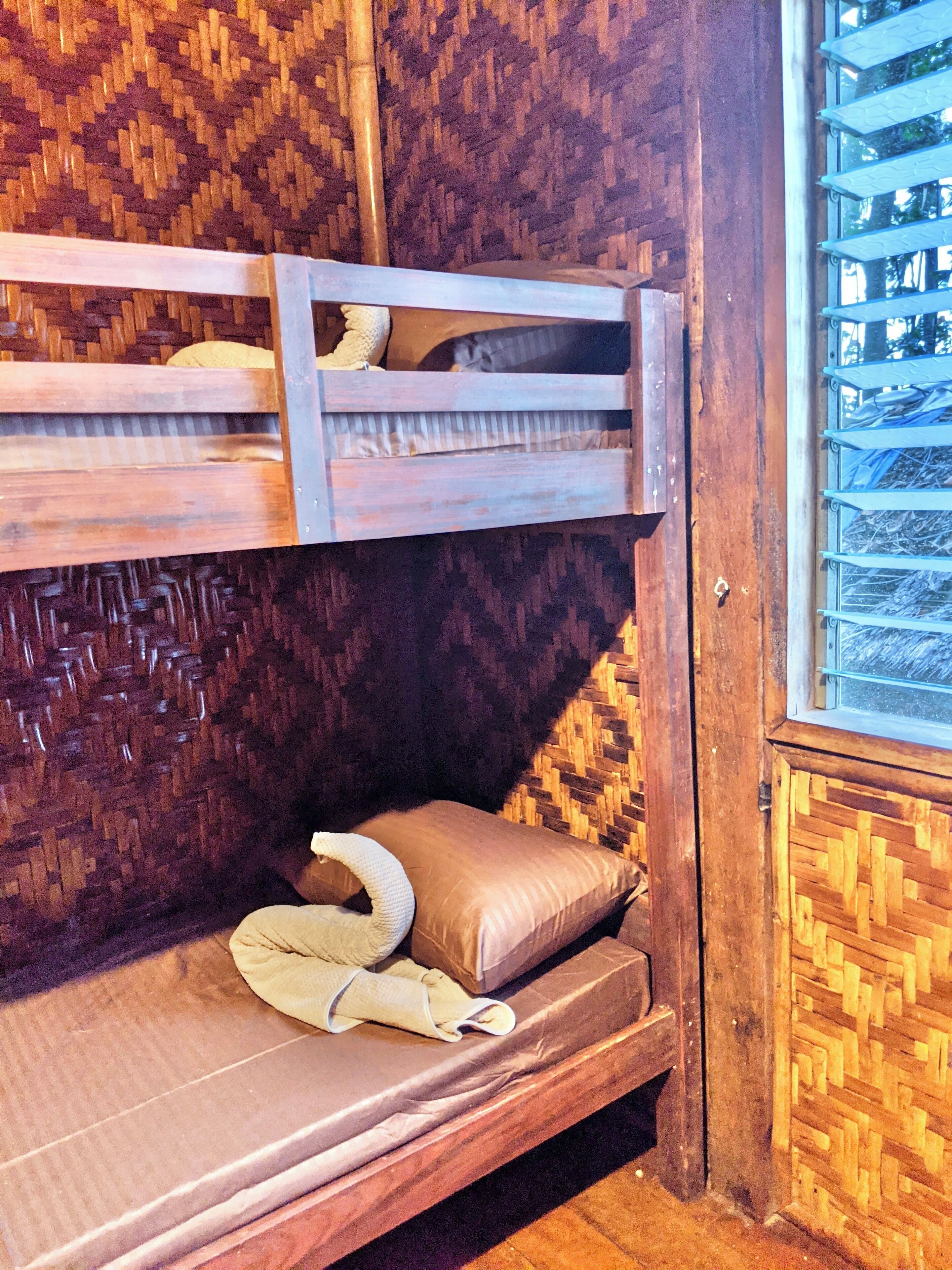 A bunk bed with a woven headboard and a window with a metal grill.