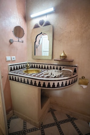 A bathroom with a curved sink, a large mirror, and a decorative tile pattern.