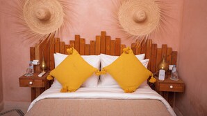 A bed with a wooden headboard, two yellow pillows, and two straw hats on the wall. - Riad Miss Caracal (Marrakech)