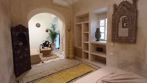 A hallway with a bed, a mirror, shelves, a plant, and a door leading to another room. - Riad Miss Caracal (Marrakech)
