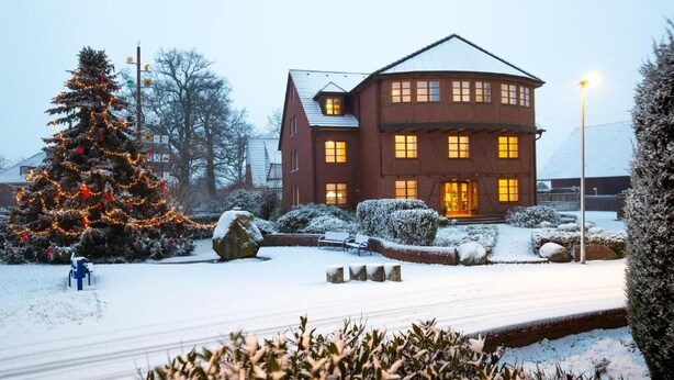 En stor byggnad i två våningar med en symmetrisk fasad, en central entré och ett snötäckt landskap med ett vackert dekorerat julgran.