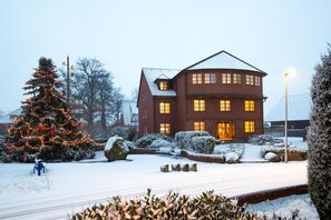 A large, two-story building with a symmetrical facade, a central entrance, and a snow-covered landscape with a decorated Christmas tree. - Hotel Alt Oesselse (Laatzen)