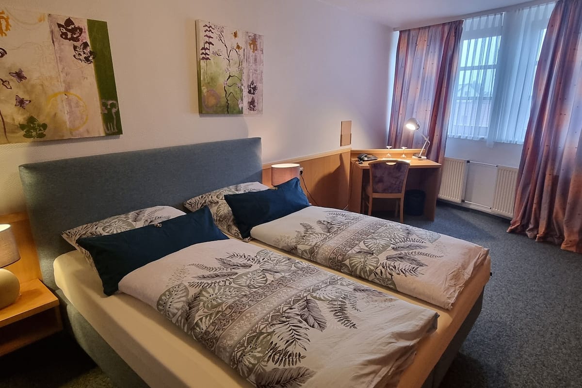 A hotel room with a bed, a desk, a chair, a TV, and artwork on the walls.