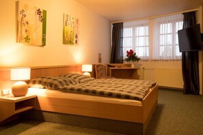 A hotel room with a bed, bedside tables, a desk, a chair, a TV, and artwork on the walls. - Hotel Alt Oesselse (Laatzen)