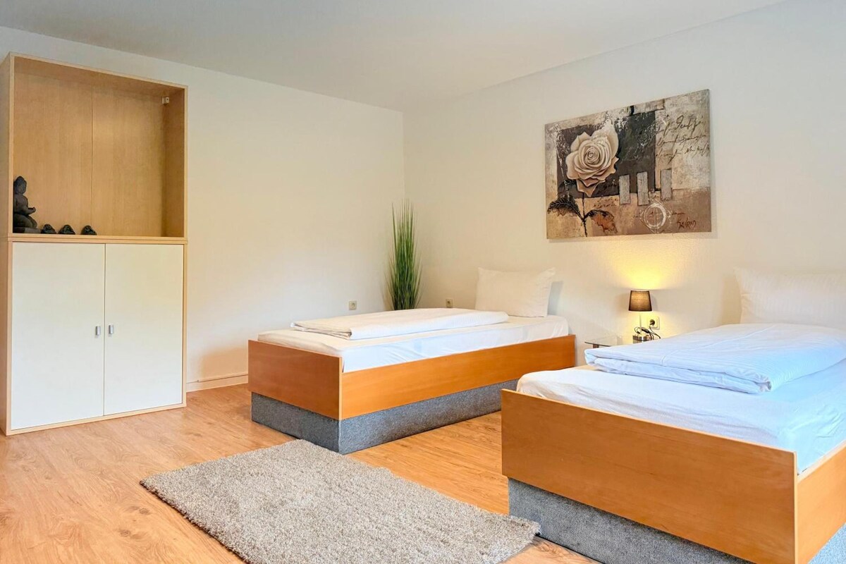 A bedroom with two beds, a wardrobe, a painting, and a bedside lamp.