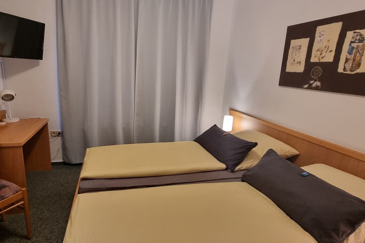 A hotel room with two beds, a desk, a chair, a flat-screen TV, and a wall with artwork.