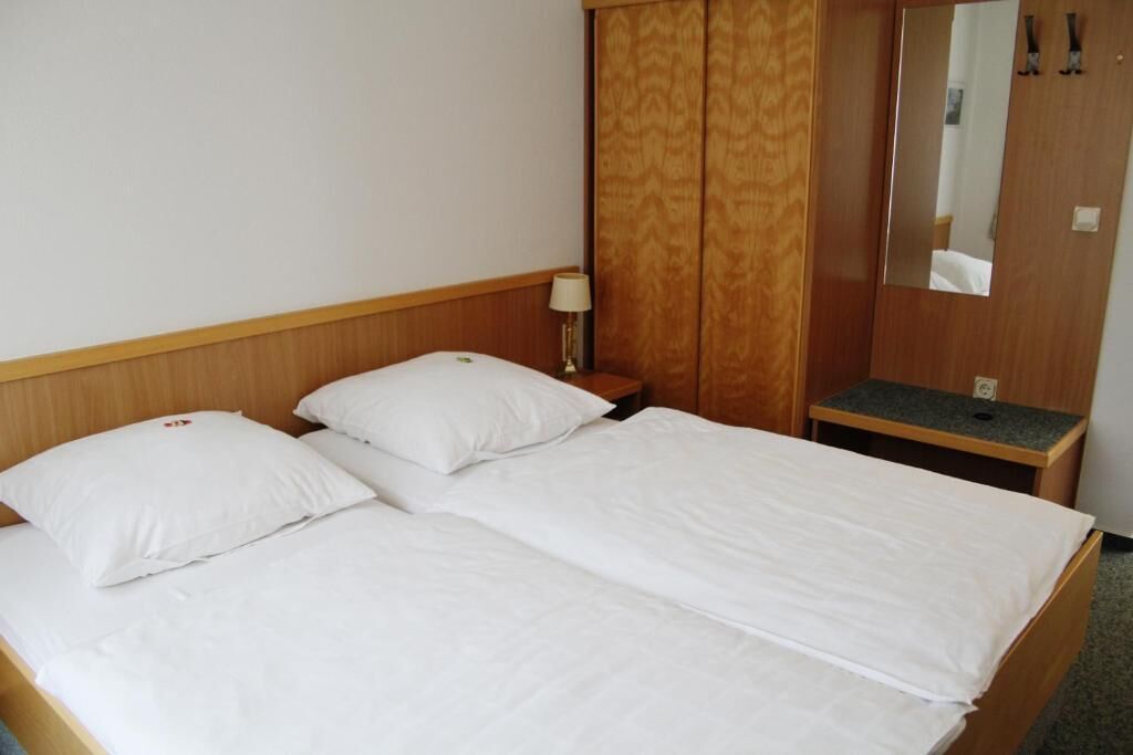 A hotel room with a double bed, a nightstand, a lamp, a mirror, and a wardrobe.