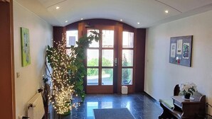 En rymlig entréhall med ett stort fönster, en receptionsdisk och en dekorativ växt.