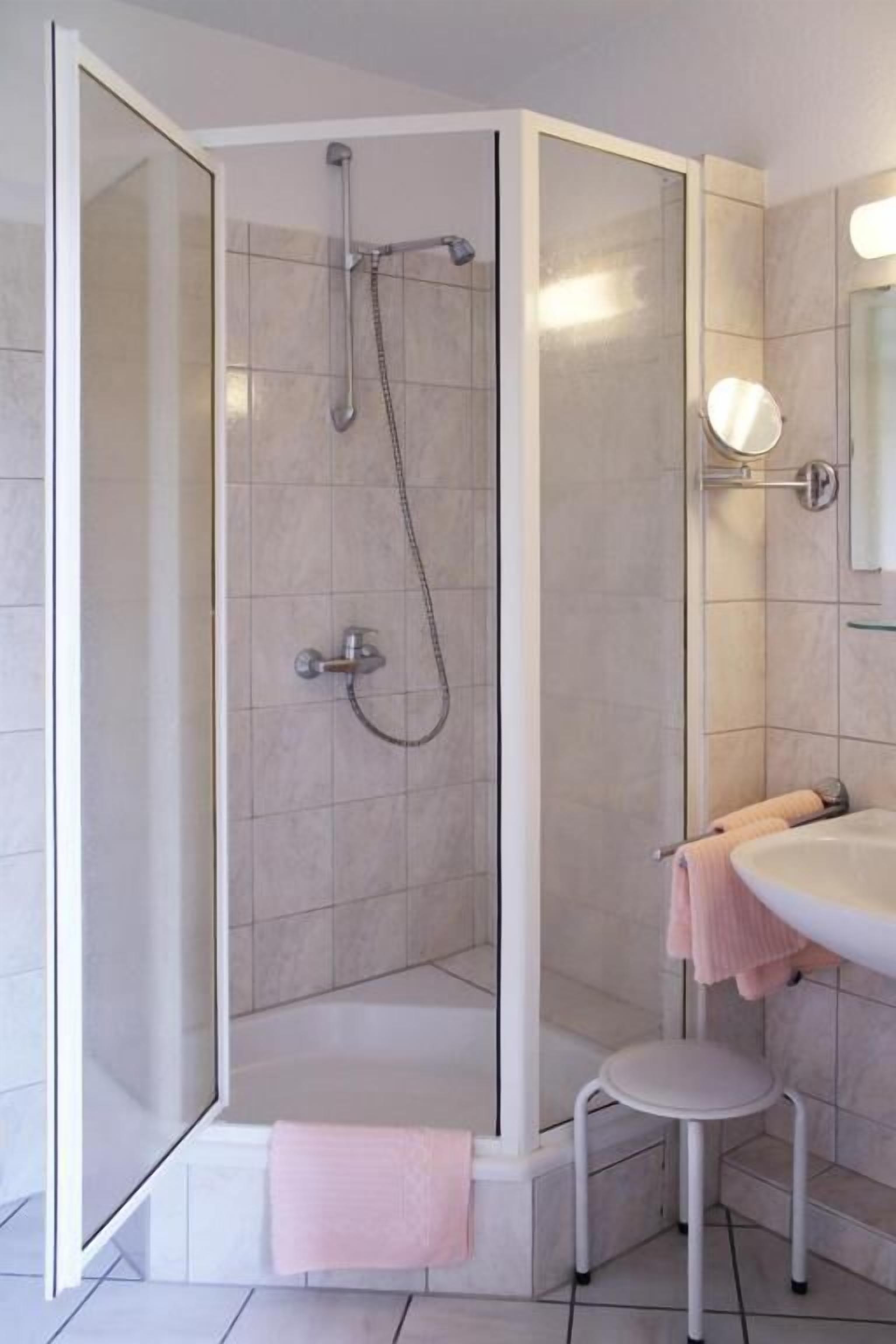 Ein modernes Badezimmer mit einer begehbaren Glasdusche, einem weißen Waschbecken und einem kleinen Hocker.