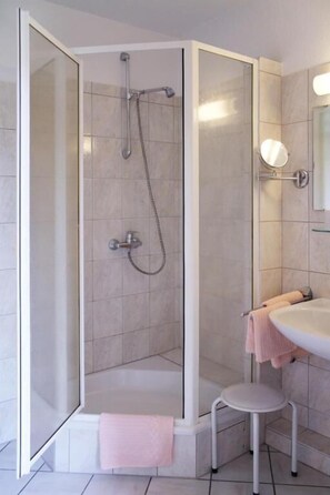 A modern bathroom with a glass-enclosed shower, a white sink, and a small stool. - Hotel Alt Oesselse (Laatzen)