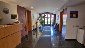 En hotelllobby med en receptionsdisk, en växt, ett stort träskåp och en dörr som leder till ett annat rum.