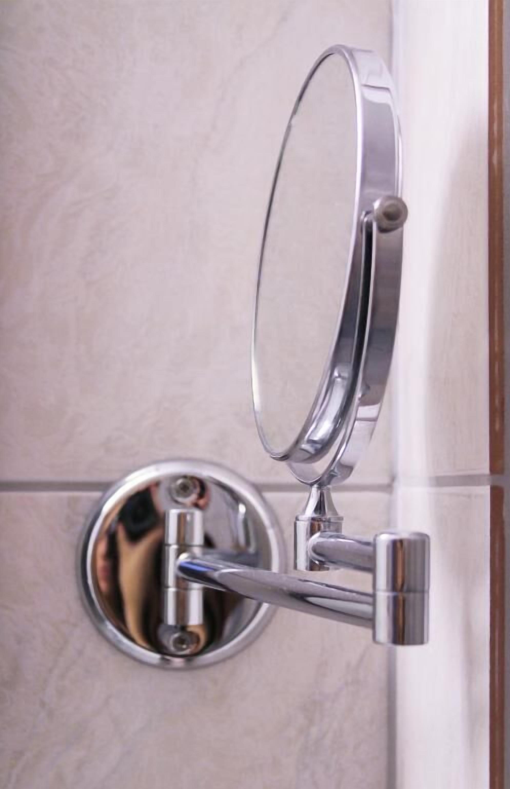Un miroir de salle de bain avec un cadre en chrome, fixé au mur au-dessus d’un lavabo rond.