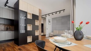 Una cocina moderna con armarios blancos y negros, un comedor con mesa de madera, y una sala de estar con sofá y un jarrón de tulipanes.