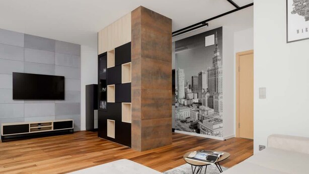 Una sala moderna con un televisor de pantalla plana grande, piso de madera, una columna central y un mural con vista a la ciudad en la pared.