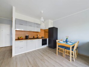 A modern kitchen with white cabinets, a black refrigerator, and a wooden dining table with blue cushions.