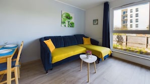 Un salon moderne avec un canapé, une petite table et une fenêtre donnant sur des immeubles.