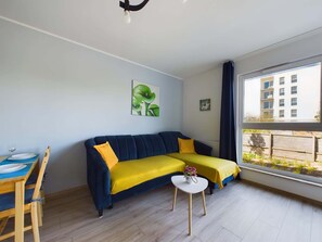 A modern living room with a sofa, a small table, and a window with a view of buildings.
