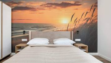 A bedroom with a large bed, two bedside tables, and a wall mural of a sunset over the ocean.