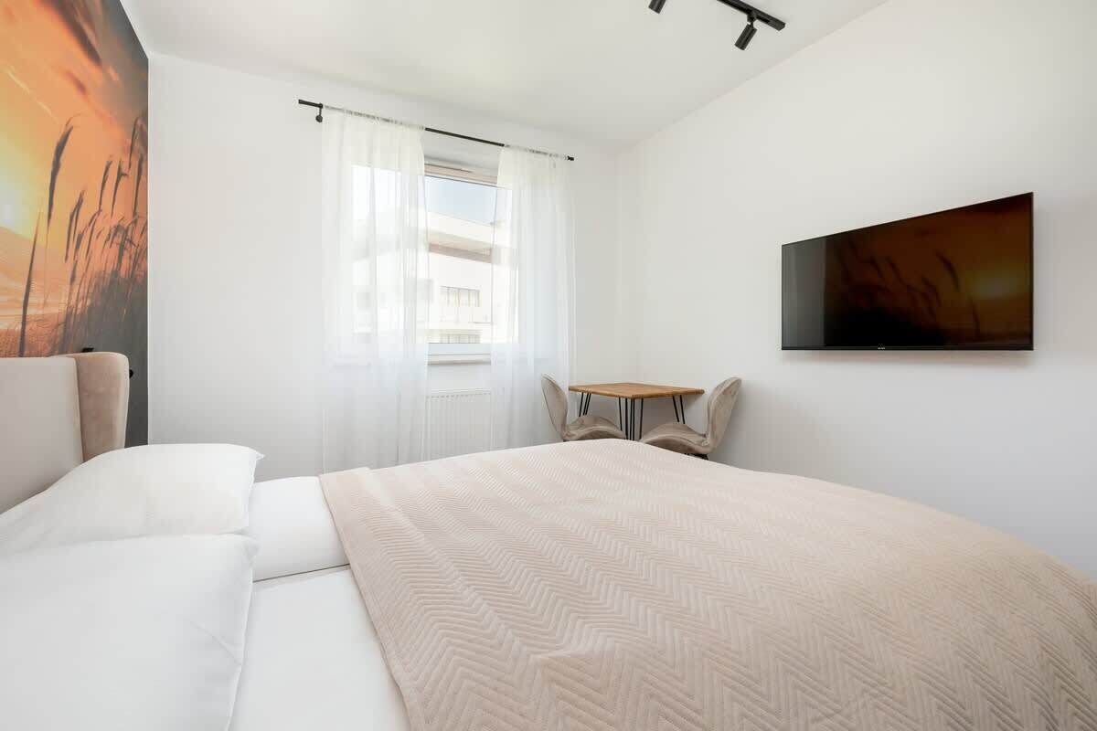 Une chambre d’hôtel avec un lit, une télévision, une fenêtre avec des rideaux, une petite table et une chaise.