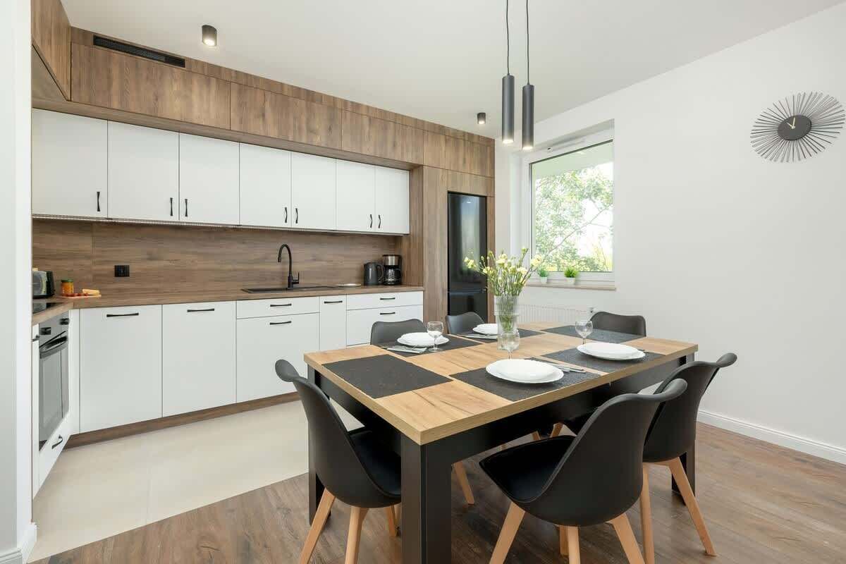 A modern kitchen with white cabinets, a wooden countertop, and a dining area with a wooden table and black chairs.