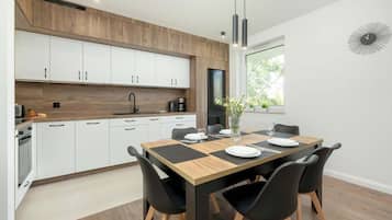 A modern kitchen with white cabinets, a wooden countertop, and a dining area with a wooden table and black chairs.