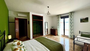 A bedroom with a bed, a dresser, a mirror, a window with curtains, and a door leading to another room.