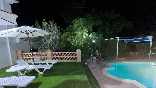 Un patio trasero con piscina, sillas de descanso blancas y un área de patio cubierta.