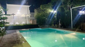 A swimming pool with a clear edge, surrounded by a concrete deck. There are lounge chairs and umbrellas in the background, suggesting a resort setting.