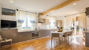 A modern kitchen with a large island, stainless steel appliances, and a dining area with a table and chairs. - Villa Olive Grove immersed in unspoilt nature (Sardegna)