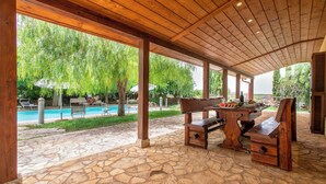 An outdoor patio with stone flooring, wooden furniture, and a view of a swimming pool. - Villa Olive Grove immersed in unspoilt nature (Sardegna)