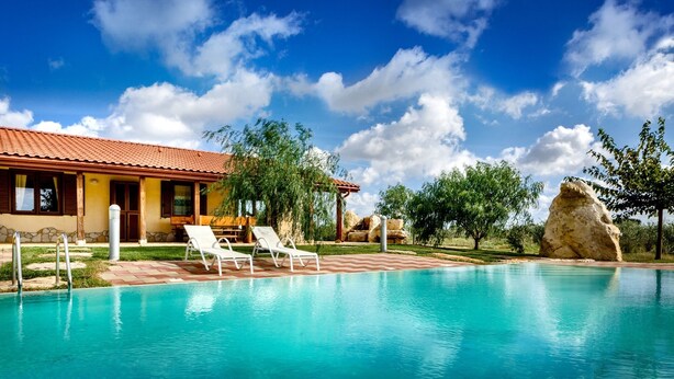 A swimming pool with lounge chairs, a stone building with a tiled roof, and a clear blue sky. - Villa Olive Grove immersed in unspoilt nature (Sardegna)