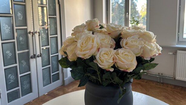 A room with a large window, a door with frosted glass panels, and a vase with white roses on a table.