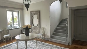 A dining area with a round table, chairs, a vase with flowers, a large mirror, and a staircase.