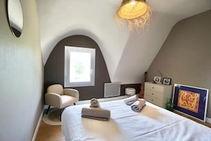 A bedroom with a bed, a chair, a desk, a window, and a wall-mounted heater.