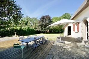 An outdoor dining area with a table and chairs, a wooden deck, and a building with a thatched roof.
