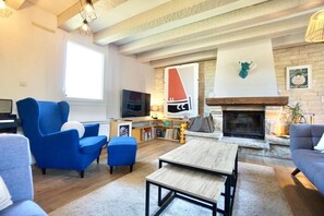A living room with a fireplace, blue armchairs, a television, and a bookshelf.