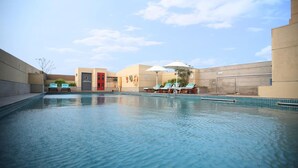 A swimming pool with lounge chairs and umbrellas, surrounded by walls and a door. - BELLA VAGUES (Chennai)