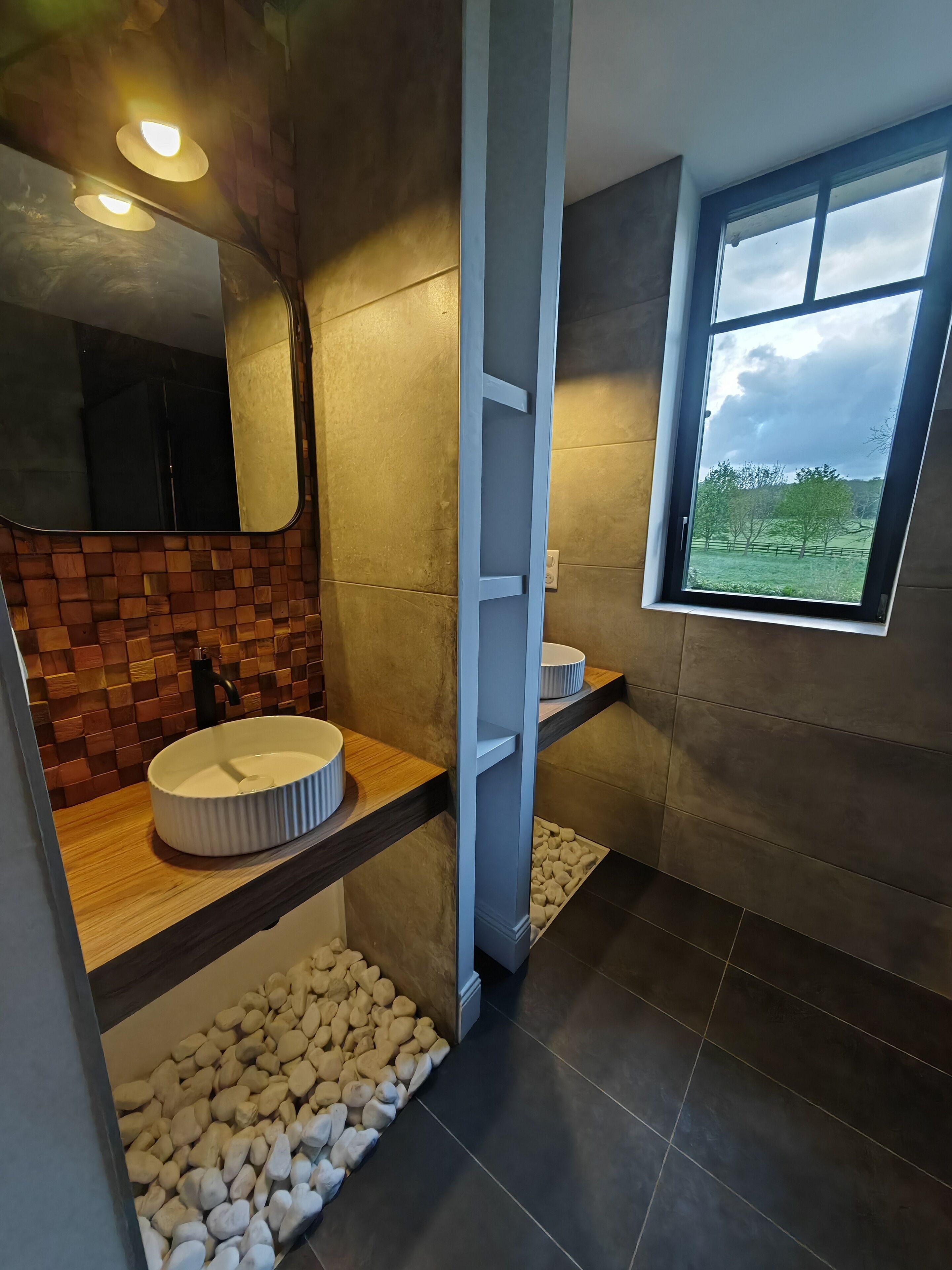 Een moderne badkamer met een grote spiegel, een rond wastafel en een raam met uitzicht op bomen.