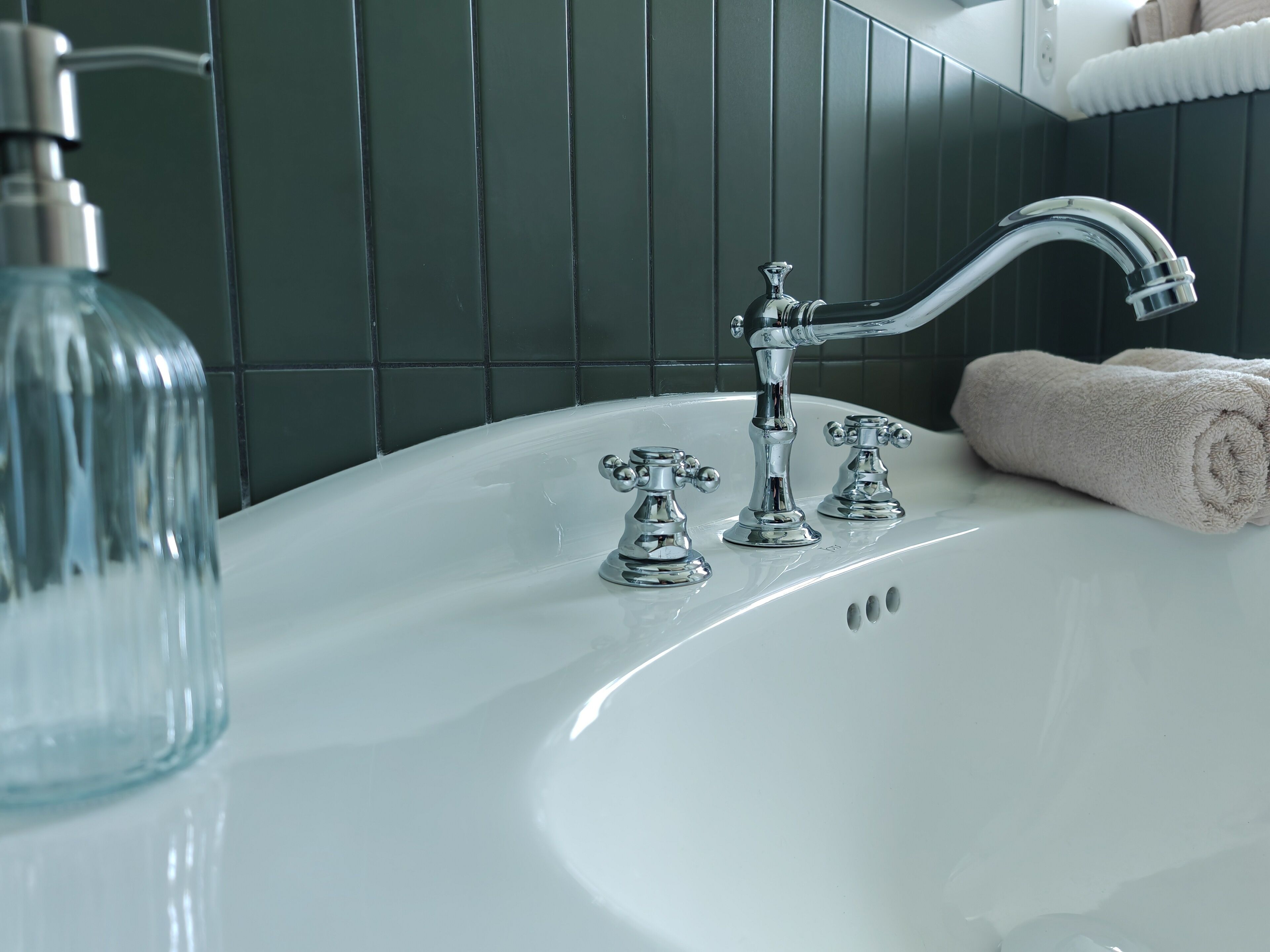 A bathroom with a white sink, two chrome faucets, and a towel on the side.