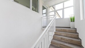 Eine Treppe mit weißen Geländern und Holzbodenstufen führt zu einer Zwischenebene mit großen Fenstern.
