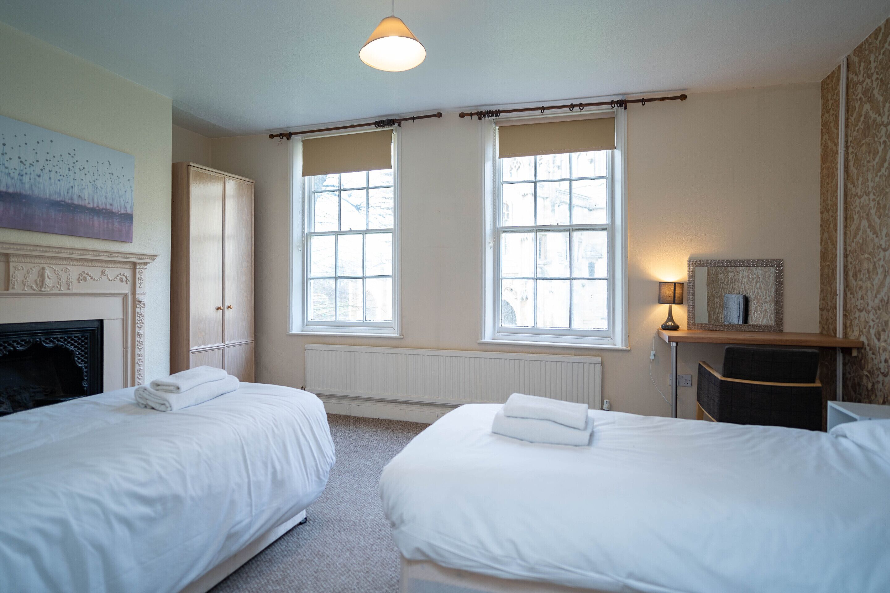 A hotel room with two beds, a fireplace, a large window, and a mirror.