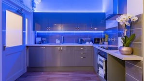 A modern kitchen with blue LED lighting, wooden cabinets, and a small island with a vase of white flowers. - Church Lane Apartments (Boston)