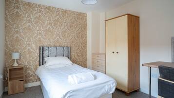 A bedroom with a bed, a wardrobe, a desk, and a nightstand.