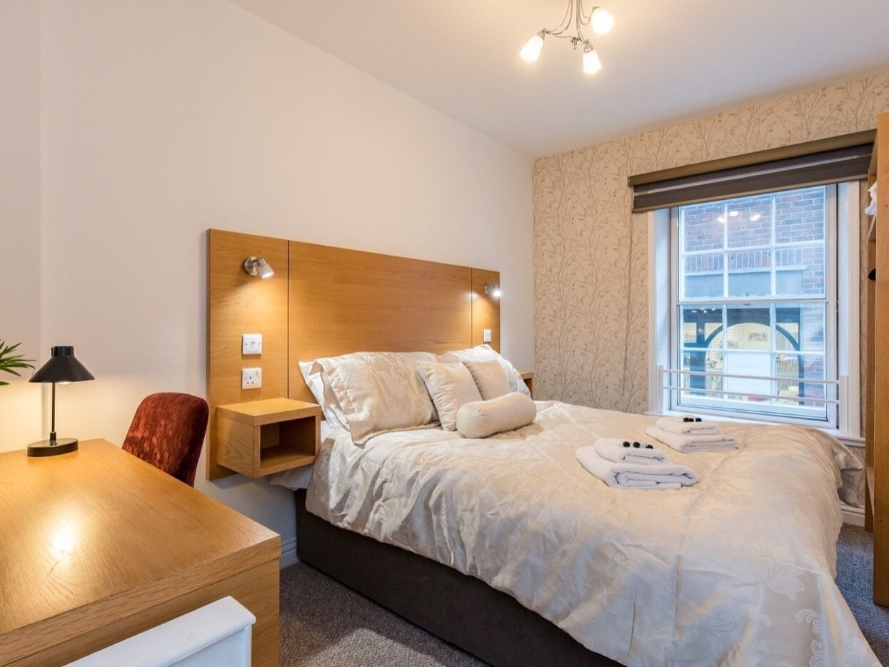 Habitación de hotel con cama, mesita de noche, lámpara y ventana con vistas.